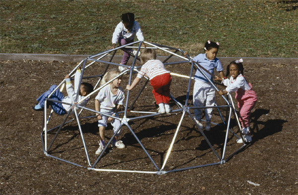 Children climbing on galvanized metal junior geo dome climber over playground mulch surface