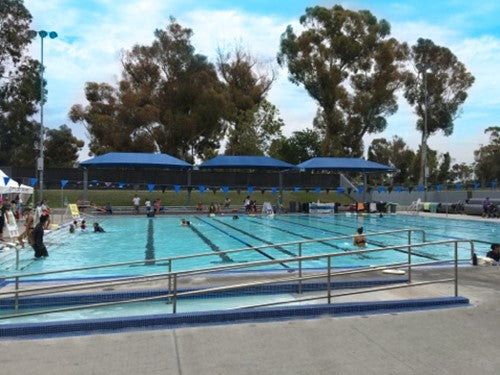 A commercial shade structure at a park with people swimming in a pool.