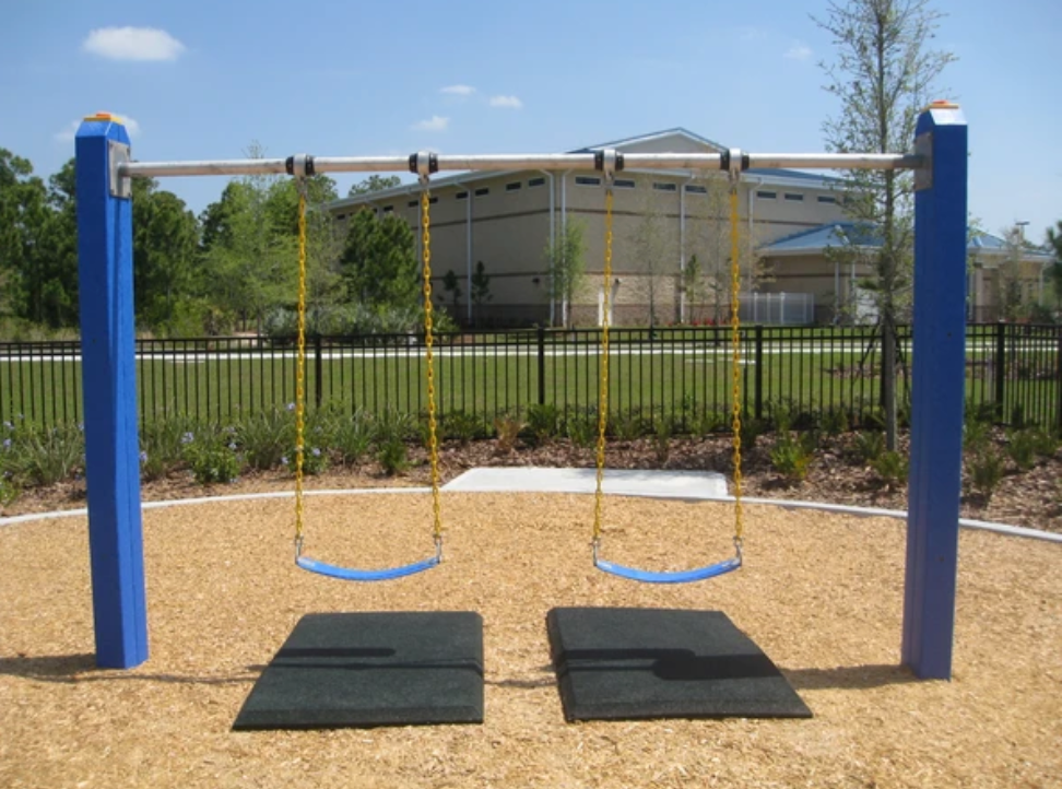 Playground swing set with two blue swings on yellow chains over black rubber safety mats on loose fill surfacing