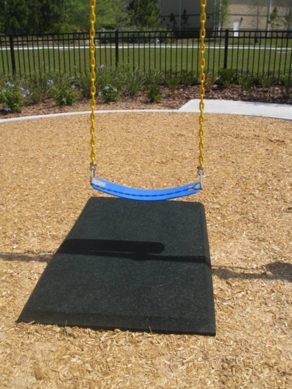 Black rubber safety mat beneath blue swing seat with yellow chains on wood chip playground surface